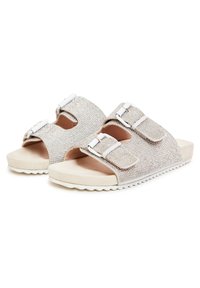 Skinner beige skydder med to justerbare remme, rhinestone detaljer og tekstureret fodseng, der har en hvid gummisål.
