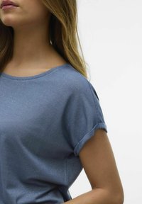 Jasnoniebieska bluzka z krótkim rękawem i okrągłym dekoltem; posiada subtelne, ukośne paski oraz podwinięte rękawy, wykonana z miękkiego, gładkiego materiału.