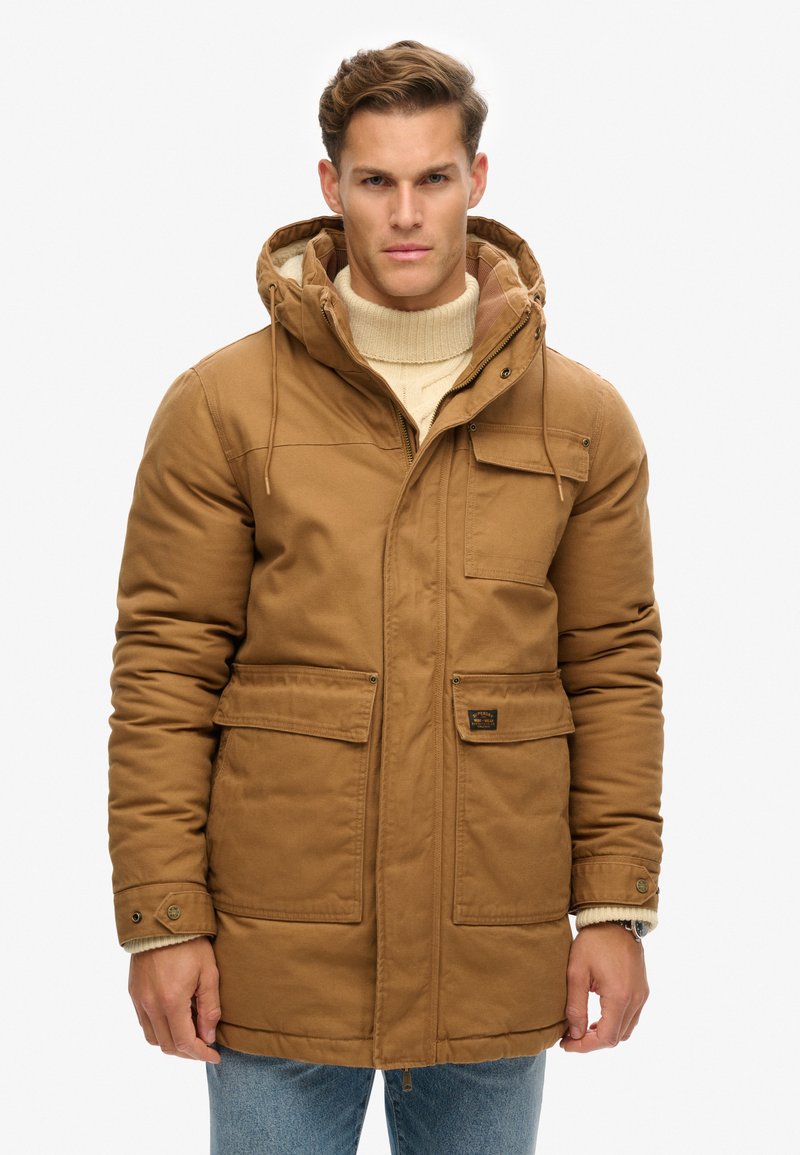 Bruine geïsoleerde parka met capuchon, voorzien van een ritssluiting en knoopsluiting, twee voorzakken en een zachte, structuurachtige binnenvoering.