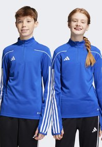 Blaue sportliche Zip-Up-Oberteile mit weißen Akzenten und drei Streifen an den Ärmeln, aus einem glatten Material gefertigt. Modelliert von zwei Jugendlichen.