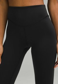 High-waisted black leggings made of smooth, stretchy material. Features a seamless design and minimalistic stitching along the waist and legs.