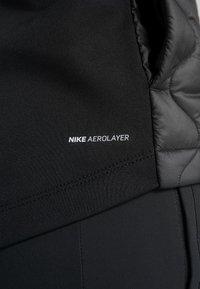 Gros plan du tissu noir Nike Aerolayer montrant des textures lisses et matelassées cousues ensemble.