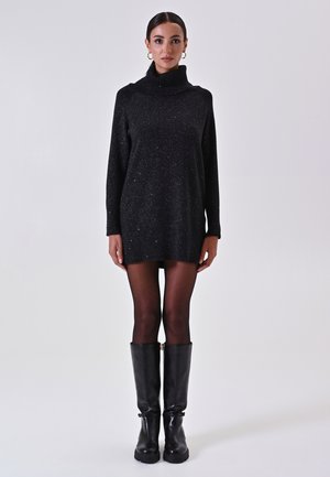 Vestito a maglia nero con colletto alto, riflessi metallici, maniche lunghe e una vestibilità ampia, abbinato a stivali in pelle nera al ginocchio.