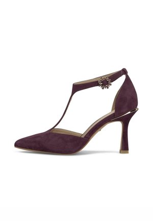 Zapato de tacón alto de ante morado con puntera puntiaguda, tira en T y hebilla adornada con joyas en la correa del tobillo.