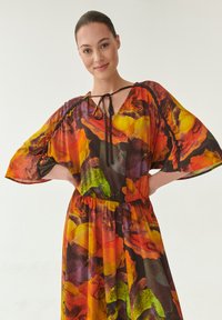 Kleurijke, vloeiende jurk met een abstract bloemenpatroon in tinten van oranje, geel, groen en paars, met een v-hals en strikdetail.