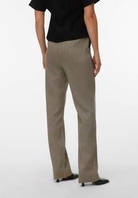 Pantalon beige sur mesure en tissu texturé, avec une coupe droite et un léger éclat. Associé à des chaussures noires à bout pointu.