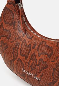 Punainen käärmeennahkakuvioitu nahkalaukku, jossa on kaareva muoto, hopeinen vetoketju ja logotunnus pohjassa. Pinta on kuvioitu suomuilla.