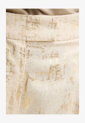 Close-up van crèmekleurige stof met een goud metallic abstract patroon en een naad die verticaal loopt, bijna in het midden.