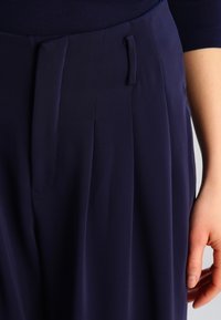 Námořnické skládací kalhoty s hladkou texturou, vybavené přední kapsou, diskrétním detailem poutka na opasek a nadčasovým střihem.