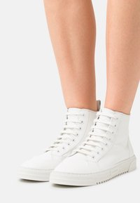 Sneakers alte bianche in pelle liscia con design con lacci, suola in gomma e un logo sottile in rilievo sul lato.