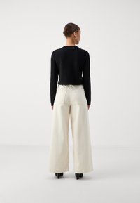 Black cropped sweater, long sleeves paired with high-waisted, wide-leg cream pants. Both pieces have a smooth texture. Black heels complete the look.