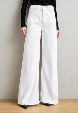 White wide-leg jeans made of denim with a high waist, featuring a button closure and belt loops, paired with black pointed heels.
