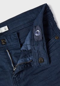 Marineblå denimbukser med synlig glidelås, knappelukking og sømdetaljer. Stoffet ser jevnt ut med en svak glans.