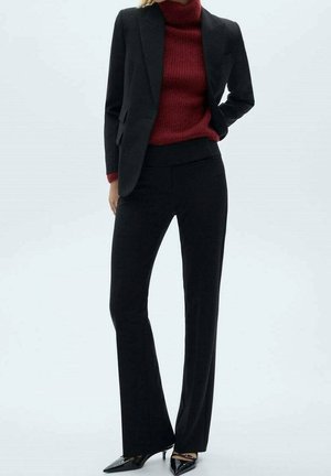 Black tailored blazer over a maroon ribbed turtleneck sweater, paired with black flared trousers. Featuring pointed black heels.