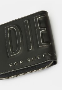 Musta vetoketjullinen lompakko, jossa on kohotettu ja painettu teksti "DIE FOR SUCCESS" pinnallaan, esitelty valkoisella taustalla.