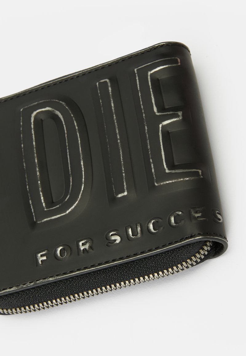Schwarze Geldbörse mit Reißverschluss und erhaben geprägtem Text "DIE FOR SUCCESS" auf der Oberfläche, auf einem weißen Hintergrund gezeigt.