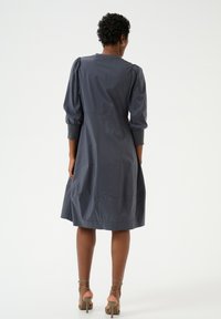 Hall sõrmedega, põlvepikkune hall kleit, millel on puhvitud varrukad ja sügavalt istuv vöökoht, valmistatud siledast kangast. Omab lihtsat, puhtat disaini ja minimaalset kaunistust.