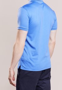 Polo shirt blu a maniche corte in un tessuto morbido e liscio. Presenta un colletto, fessure laterali e dettagli di cucitura a contrasto.
