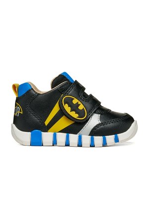 Basket bébé noire avec logo Batman sur la bride, accents jaunes et bleus, semelle blanche avec blocs bleus.