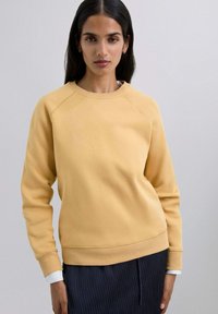Żółta bawełniana bluza z okrągłym dekoltem, rękawami raglanowymi, ściągaczami przy mankietach oraz luźniejszym krojem, w połączeniu z paskowaną dolną częścią.