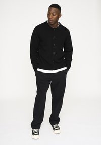 Sort strikket cardigan med knaplukning, rebede ærmer og krave, parret med sorte bukser og sorte sneakers med hvide såler.
