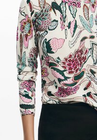 Top a maniche lunghe stampato floreale in crema con accenti rosa e verdi. Presenta polsini a costine e un design aderente, con un fondo nero a contrasto.