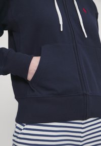 Marinblå zip-up hoodie i bomullsblandning med vit dragsko, kängurufickor och ribbad mudd. Randiga byxor under har blåa och vita ränder.