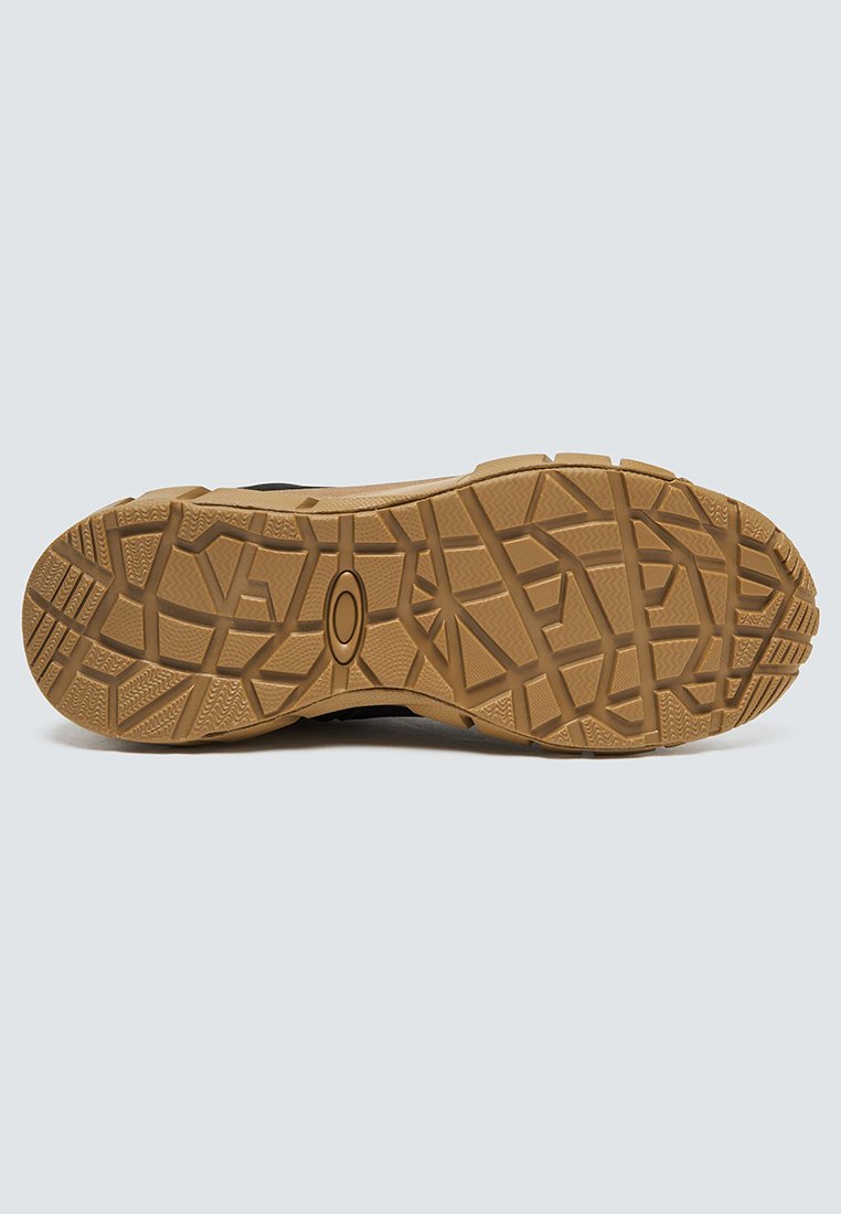 Suela de un zapato marrón para exterior con patrones de dibujo geométrico profundos para tracción, mostrada contra un fondo claro y liso.