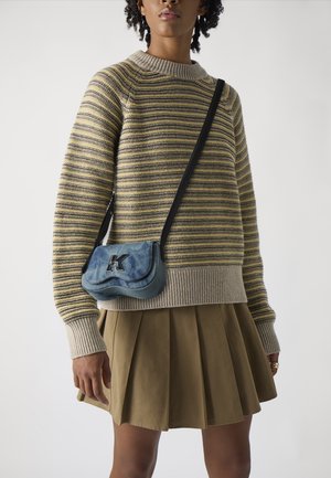 Striped knit sweater in yellow and gray, paired with a pleated khaki skirt. A small blue bag featuring a black "K" logo is worn crossbody.