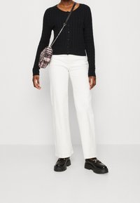 Czarny prążkowany sweter na guziki, zestawiony z białymi, szerokimi spodniami jeansowymi i masywnymi czarnymi butami. Mała torebka z wzorem noszona na ukos.