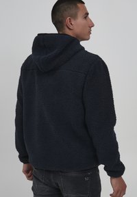 Navy blue fleece hoodie with a textured, fluffy exterior, front zip, and a hood. Features fitted cuffs and a relaxed fit.