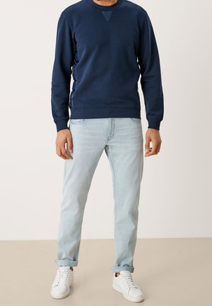 Granatowa bawełniana bluza z okrągłym dekoltem i ściągaczami przy rękawach, zestawiona z jasnoniebieskimi jeansami i białymi sportowymi butami.