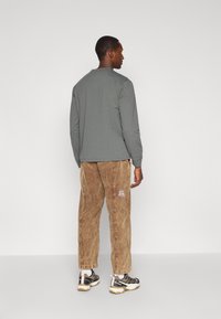 Szary top z długim rękawem i okrągłym dekoltem, zestawiony z luźnymi brązowymi spodniami z kordurowej tkaniny z logo. W zestawie także czarno-białe tenisówki.