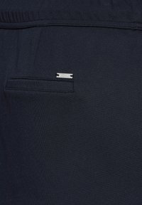 Pantalons en tissu bleu marine présentant une texture lisse, une taille élastique et un petit logo en métal sur la poche arrière.