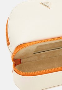 Cremefarvet pung lavet af tekstureret materiale med en orange lynlås. Indvendigt har den et blødt stoffor og en slot til opbevaring. Brandlogoet er synligt.