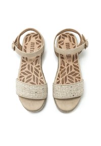 Sandalias beige con una correa de tela texturizada, hebilla ajustable en el tobillo y suela con un diseño estampado de hojas. Construcción suave y ligera.