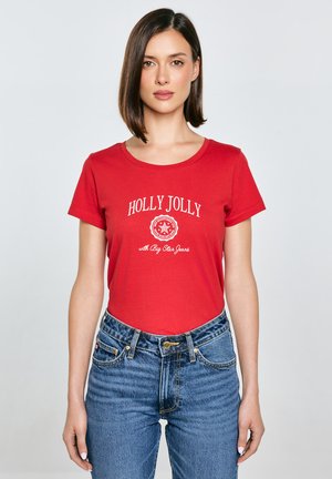 Červené bavlněné tričko s kulatým výstřihem a bílým potiskem "HOLLY JOLLY", kombinované s vysokými modrými džínami. Jednoduchý design.