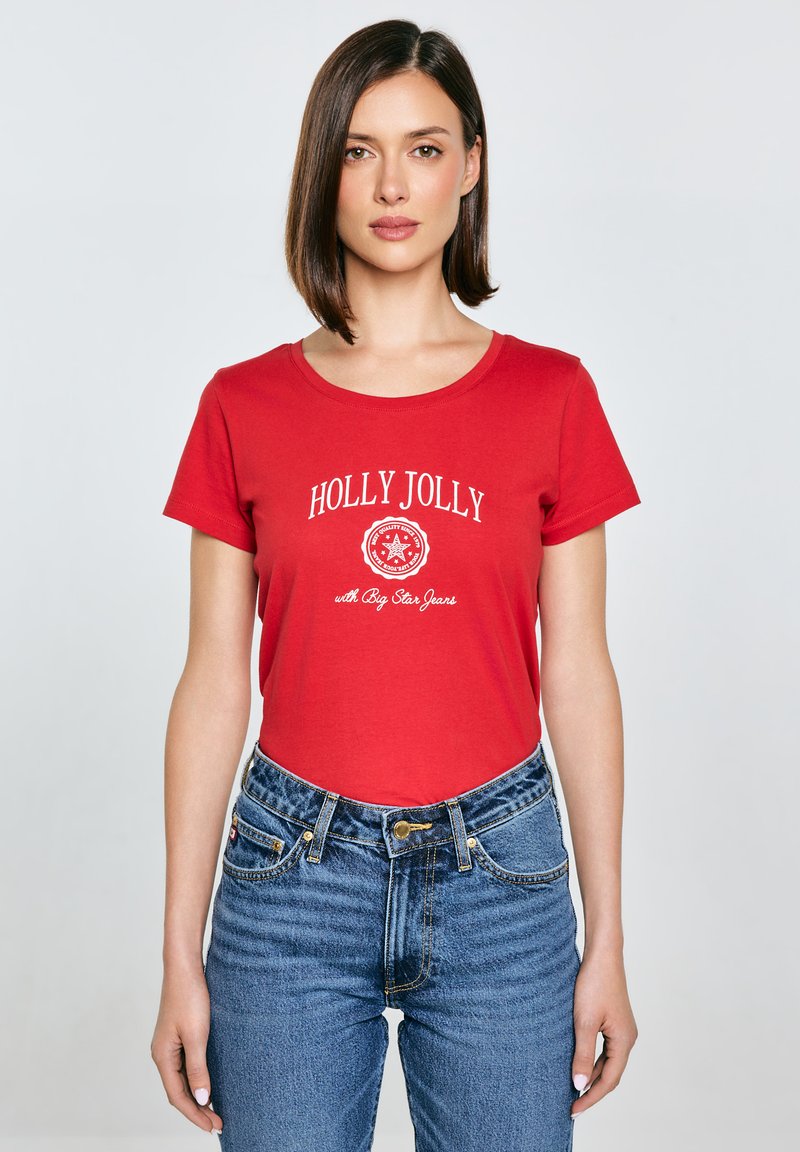 Červené bavlněné tričko s kulatým výstřihem a bílým potiskem "HOLLY JOLLY", kombinované s vysokými modrými džínami. Jednoduchý design.