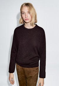 Maglione a maglia marrone scuro con scollatura rotonda e maniche lunghe, abbinato a pantaloni in suede beige. Design semplice, texture morbida.