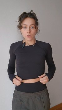 Must musta pika varrukaga lühike top, millel on vormiv lõige ja tekstuuriga kangas, kombineeritud lahtiste oliivroheliste pükstega, neutraalse taustaga.