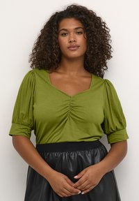 Olijfgroen, korte mouwtop met een V-hals en geraffineerde details in het midden. Draag het met een zwarte, hoge taille, gestructureerde rok.