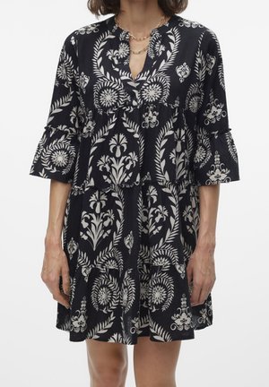 Sukienka w czarno-kremowy wzór z rękawami do połowy łokcia, falbanami w warstwach i kołnierzykiem z wycięciem, zdobiona motywami botanicznymi.