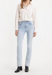 Světlé modré džíny s vysokým pasem v kombinaci s bílou košilí na knoflíky. Džíny mají slim fit střih, zatímco košile má kapsu na hrudi.