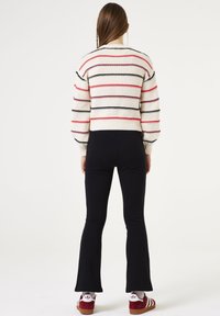 Suéter blanco de punto con franjas horizontales rojas y negras. Combinado con pantalones de campana negros. El calzado cuenta con detalles en rojo y blanco.