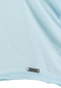 Jasnoniebieska tkanina z małą prostokątną metalową metką wszytą blisko dołu, na której widnieje nazwa marki "Key Largo".