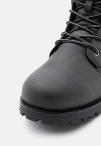 Crne kožne čizme s zaobljenim vrhom, teksturiranom površinom, vezicama i robusnim crnim gumiranim đonom s dubokim utorima.