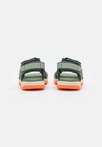 Grå tekstil sandaler med justerbare stropper, med en oransje såle og en polstret såle. Teksturerte detaljer på stroppene.