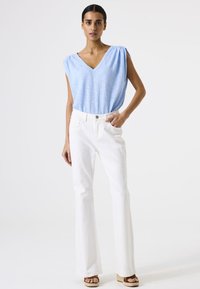 Top azul claro con escote en V y hombros fruncidos; combinado con jeans blancos de campana; sandalias de plataforma en tonos neutros; diseño sencillo, textura suave.