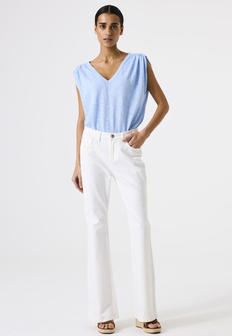 Top azul claro con escote en V y hombros fruncidos; combinado con jeans blancos de campana; sandalias de plataforma en tonos neutros; diseño sencillo, textura suave.