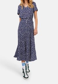 Robe marine avec imprimé floral blanc, manches courtes, boutonnière à l'avant et ourlet évasé. Assortie avec des baskets vertes et des chaussettes à rayures bleues.